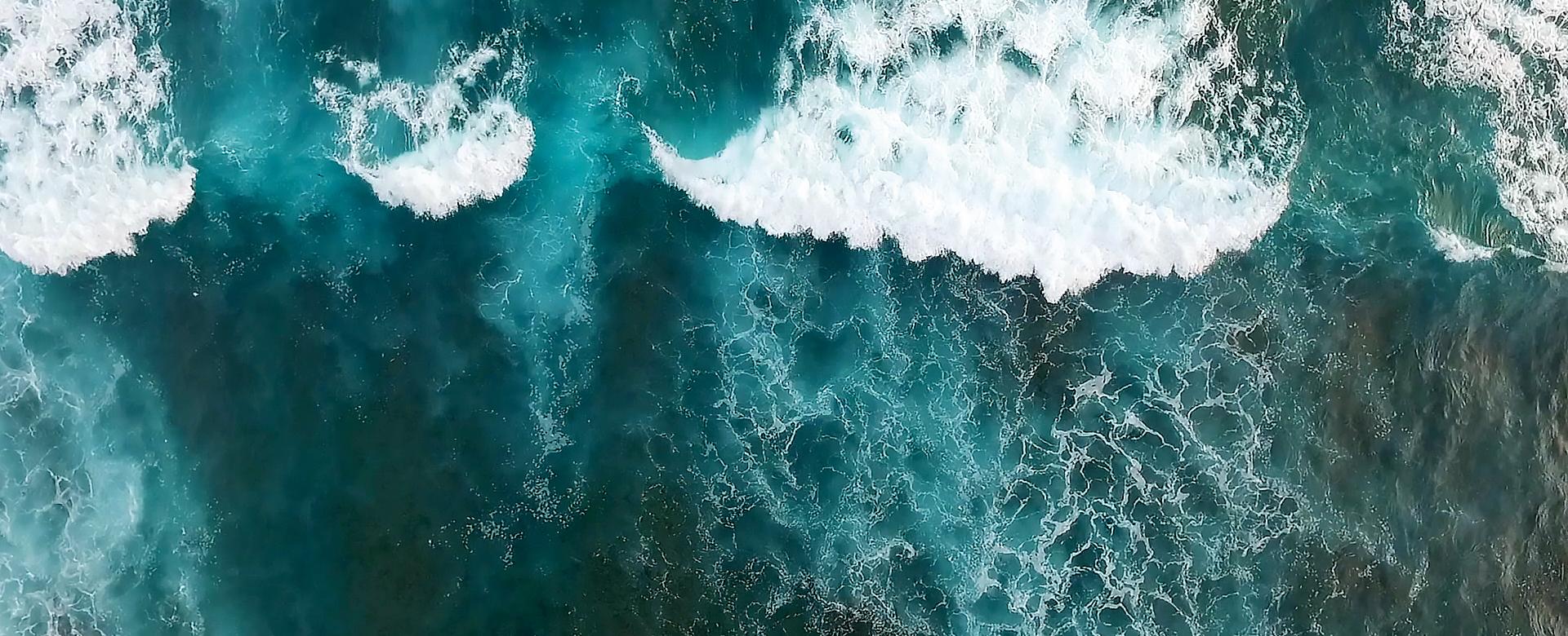 BEAUTY SOLUTIONS Kosmetikmarken | PHYTOMER | Imagebild Meer | © PHYTOMER Codif International Ein Luftbild dynamischer Meereswellen, die sich mit Schaumkronen über das türkisfarbene Wasser ausbreiten. Das Bild vermittelt die rohe Kraft und Schönheit der Natur, während die brechenden Wellen ein faszinierendes Muster erzeugen.