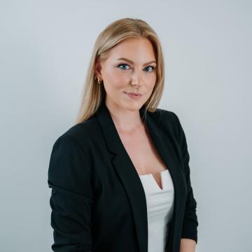 BEAUTY SOLUTIONS Team | Marketing & Communication Manager | Lisa Jarec | © BEAUTY SOLUTIONS | Martin Hofmann Fotografie Ein professionelles Porträt einer jungen Frau mit blonden Haaren in einem schwarzen Blazer und weißem Top. Vor einem neutralen Hintergrund posierend, vermittelt sie einen selbstbewussten und kompetenten Eindruck. Perfekt für geschäftliche Profile oder professionelle Darstellungen.