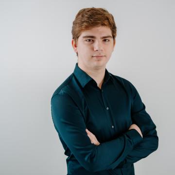 BEAUTY SOLUTIONS Team | E-Commerce Manager | Ronald Menard | © BEAUTY SOLUTIONS | Martin Hofmann Fotografie Ein junger Mann mit verschränkten Armen steht vor einem neutralen Hintergrund. Er trägt ein dunkelgrünes Hemd und blickt selbstbewusst in die Kamera. Das Bild vermittelt ein Gefühl von Professionalität und Gelassenheit.