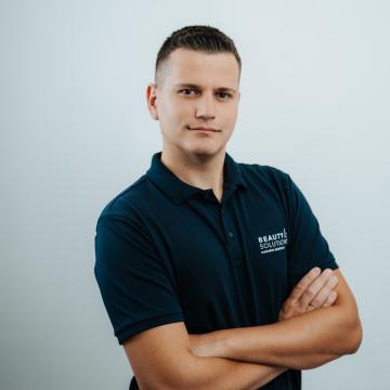 BEAUTY SOLUTIONS Team | Order Picking Specialist | Dario Gugic | © BEAUTY SOLUTIONS | Martin Hofmann Fotografie Ein selbstbewusster Mann in einem dunkelblauen Poloshirt mit verschränkten Armen. Der Hintergrund ist schlicht und hell, was den Fokus auf die Person lenkt.