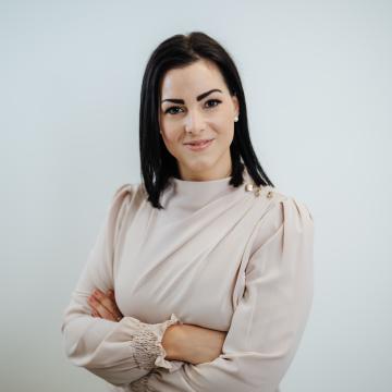 BEAUTY SOLUTIONS Team | Customer Service & Office Manager | Daniela Fantur | © BEAUTY SOLUTIONS | Martin Hofmann Fotografie Ein professionelles Porträt einer Frau in eleganter, heller Kleidung. Sie hat dunkles, schulterlanges Haar und steht mit verschränkten Armen vor einem neutralen Hintergrund. Ihr selbstbewusster Blick und die dezente Beleuchtung schaffen eine seriöse, einladende Atmosphäre.