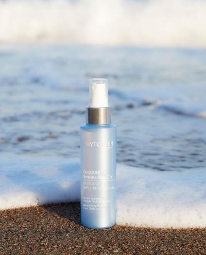 BEAUTY SOLUTIONS Kosmetikmarken | PHYTOMER | OLIGOMER® WELL-BEING Sensation | © PHYTOMER Codif International Ein erfrischendes Hautspray in einer blauen Flasche steht am Strand, umgeben von sanften Meereswellen. Die Szene verbindet Pflege und Natur und vermittelt ein Gefühl von Frische und Entspannung.